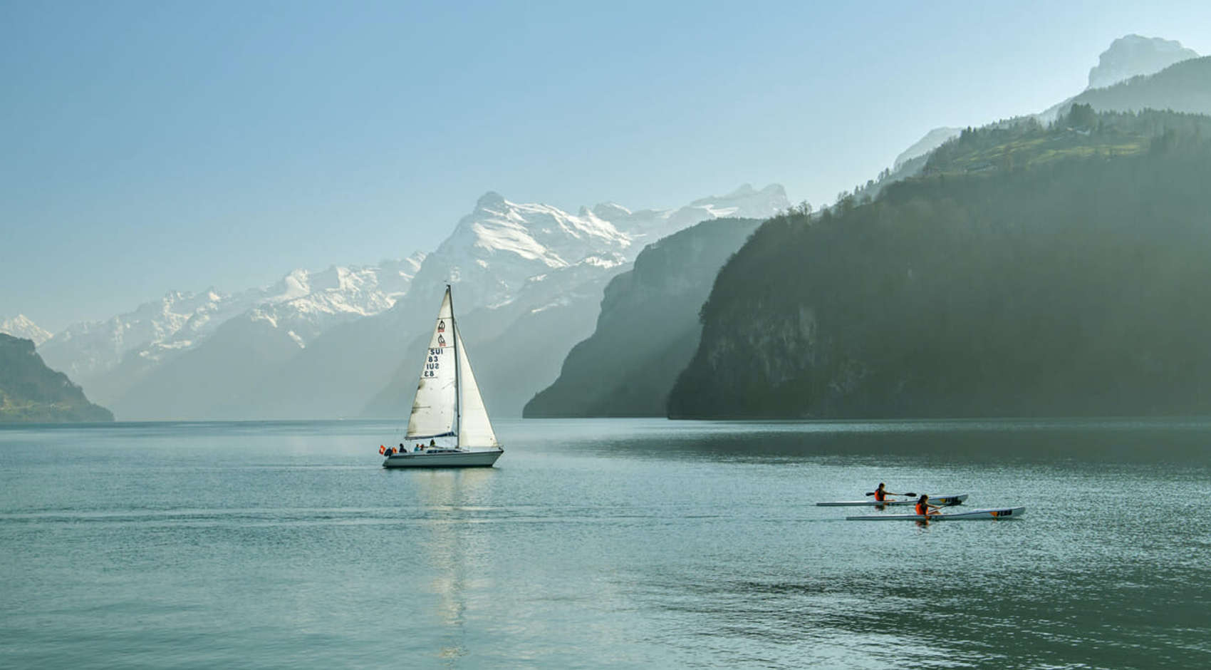 See vor bergigem Hintergrund mein einem Segelboot und zwei Ruderboten